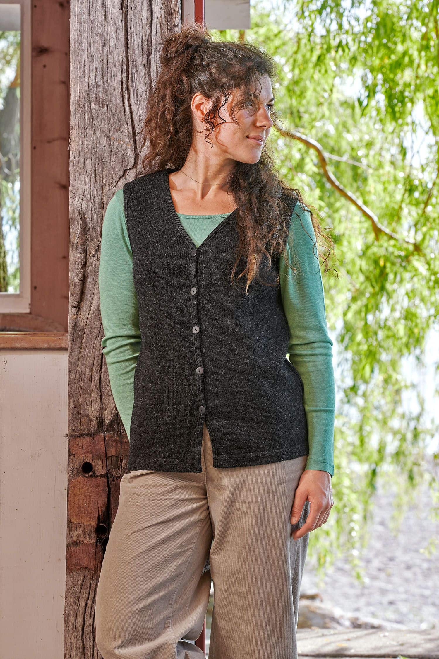 Frau trägt eine graue Strickweste ohne Ärmel aus bio Wolle (kbT) vom Finkhof mit grünem Shirt und beiger Hose