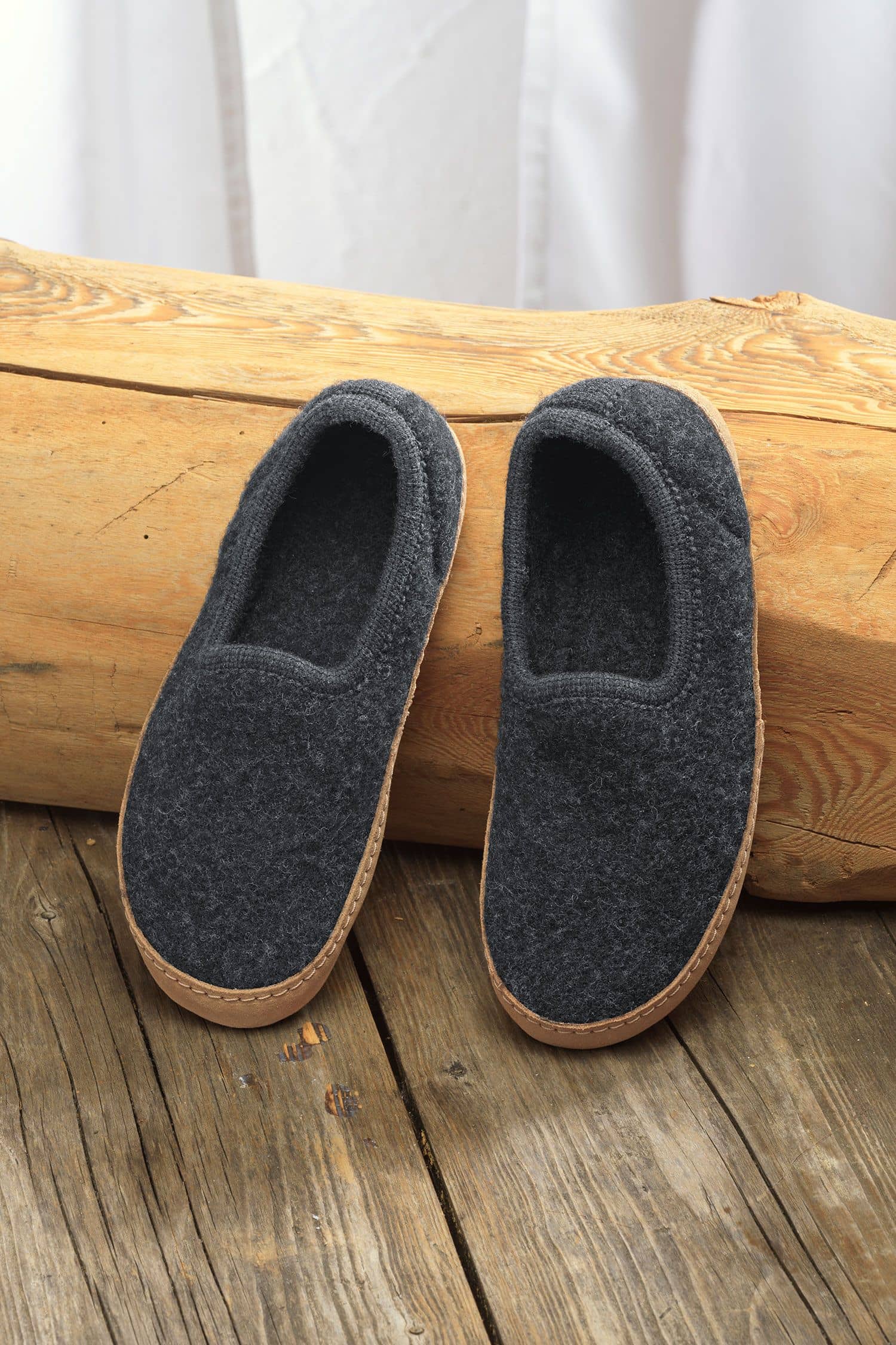 Paar dunkelgraue Finkhof Hausschuhe aus bio Wolle (kbT) und einer Sohle aus pflanzlich gegerbtem Rindsleder auf Baumstamm