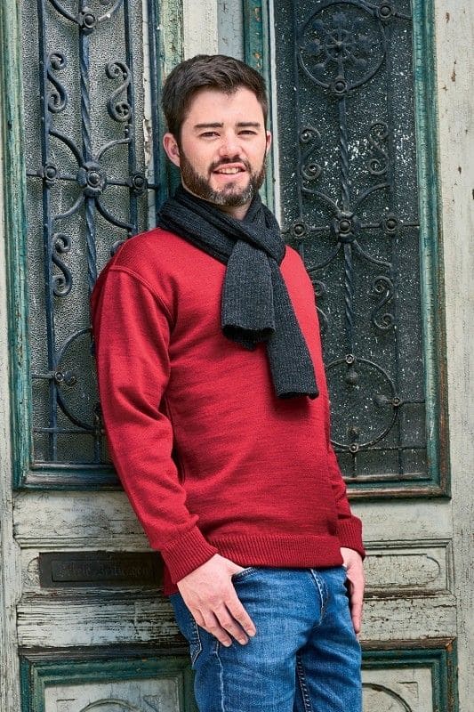 Mann lehnt sich mit rotem Rundhalspullover aus bio Wolle (kbT) vom Finkhof und grauem Schal an eine Tür