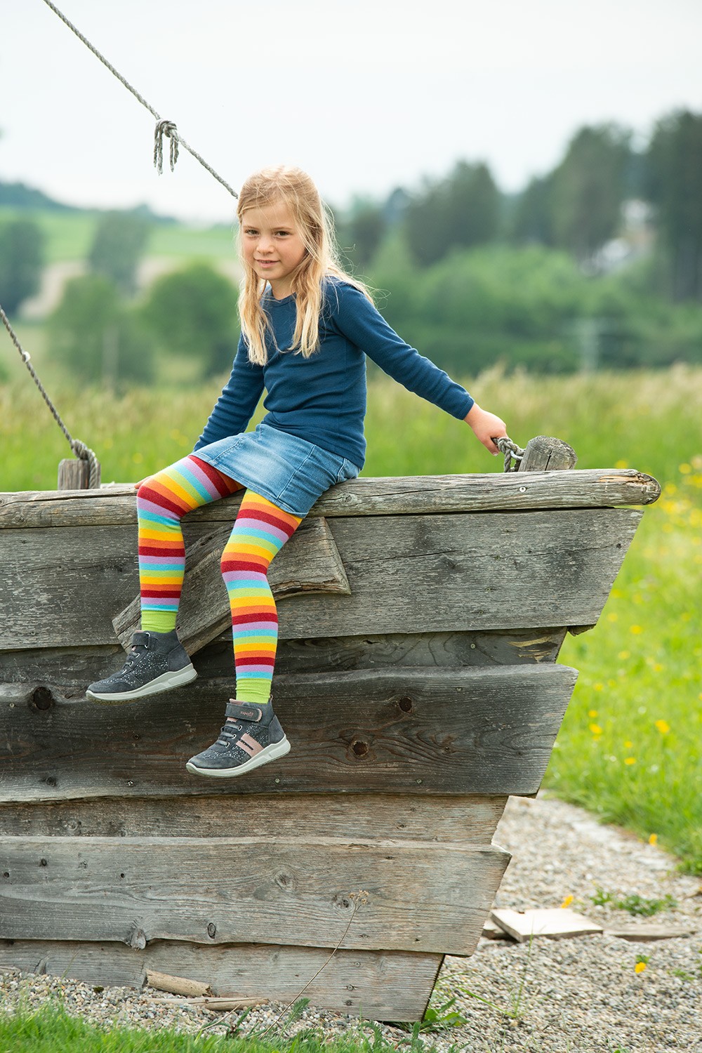 Kindershirt einfarbig Langarm mit Bio-Fasern Kind sitzt auf Holzschiff und trägt ein dunkelblaues Langarmshirt aus bio Wolle (kbT) und Seide und einen Rock