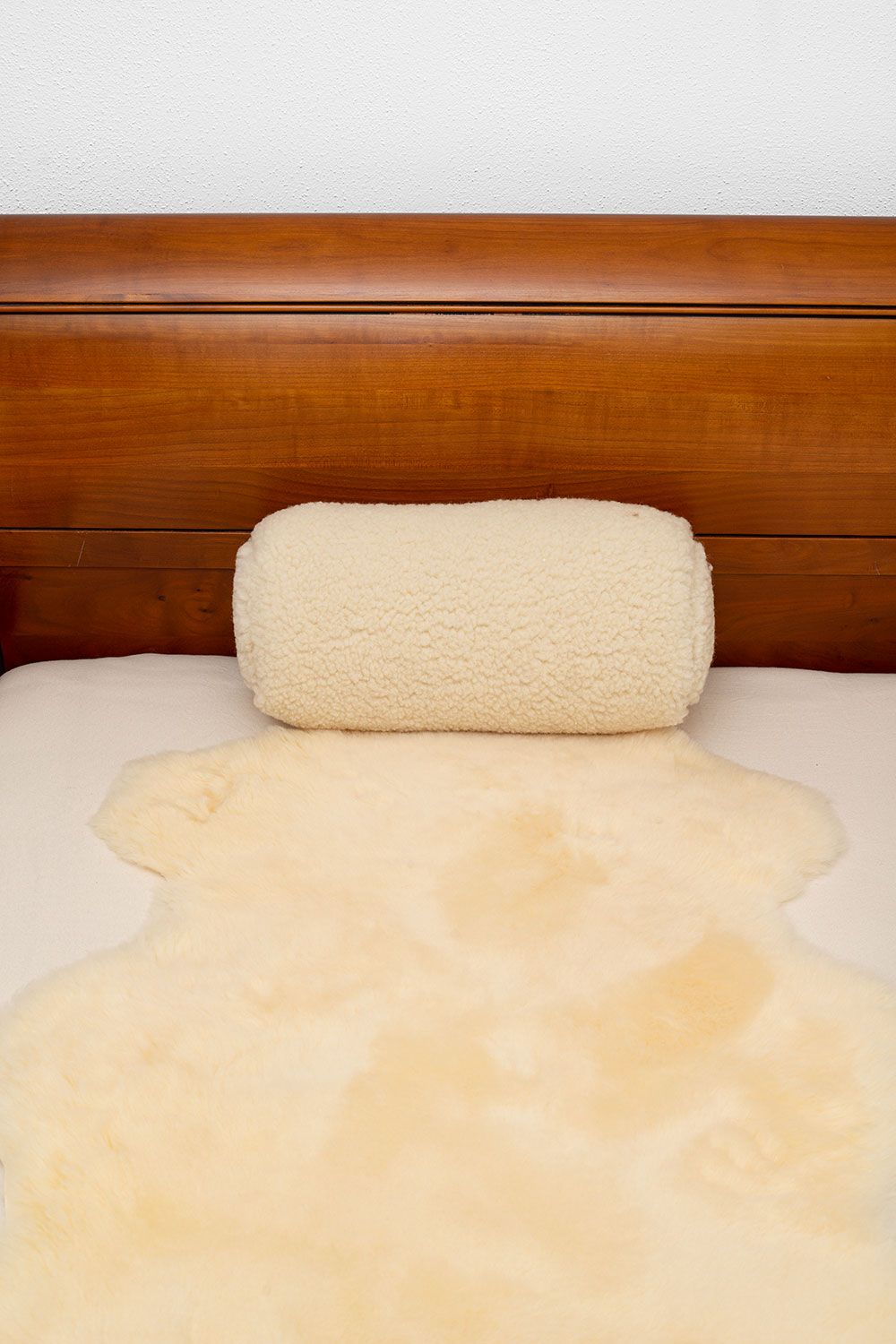 Nackenrolle in naturweiß vom Finkhof mit Wollplüschbezug aus bio Wolle (kbT) liegt auf einem Fell in einem Bett