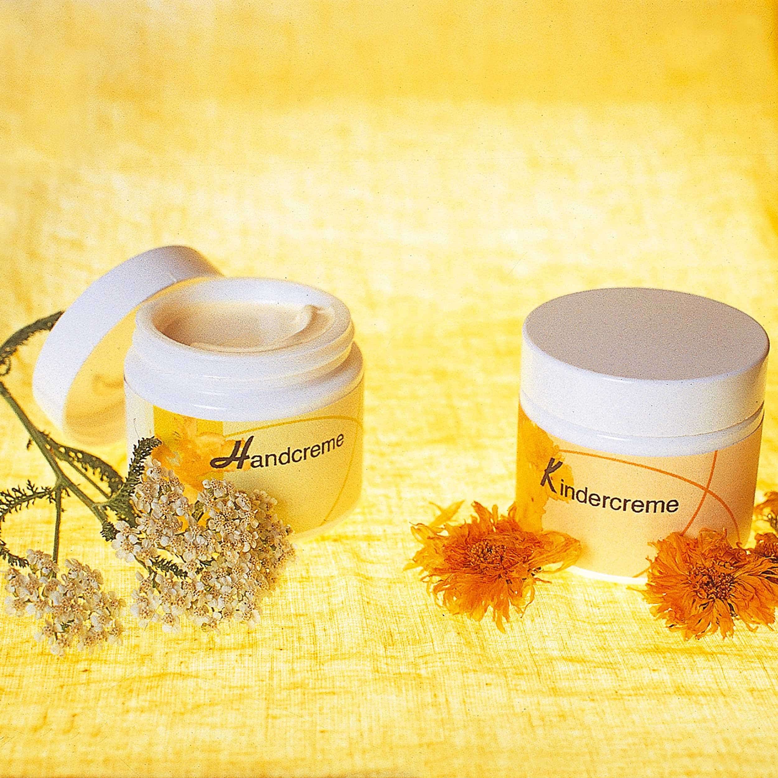 Tiegel mit Kinder- und Handcreme auf gelbem Stoff mit Blüten