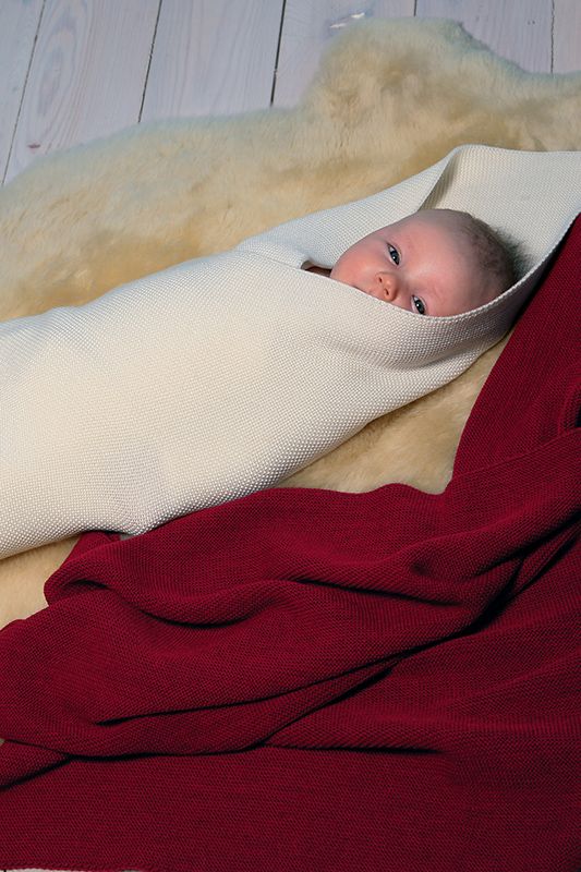 Wickeldecke rote Finkhof Wickeldecke aus bio Wolle (kbT) in 70x95 cm liegt neben eingewickeltem Baby auf Fell