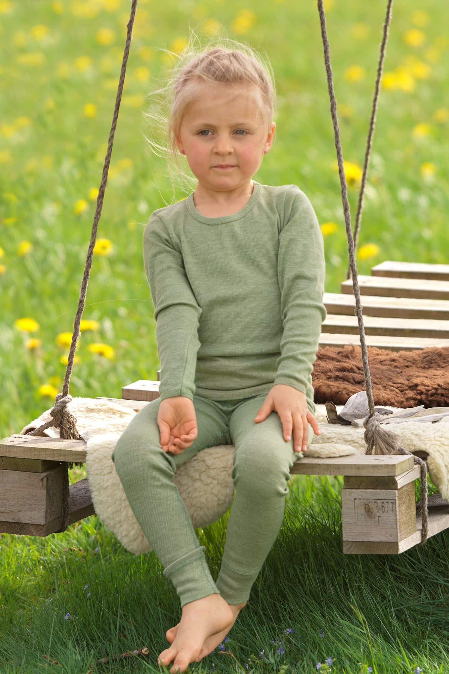 Mädchen sitzt auf Schaukel und trägt ein grünes Langarmshirt aus bio Wolle (kbT), bio Baumwolle (kbA) und Seide