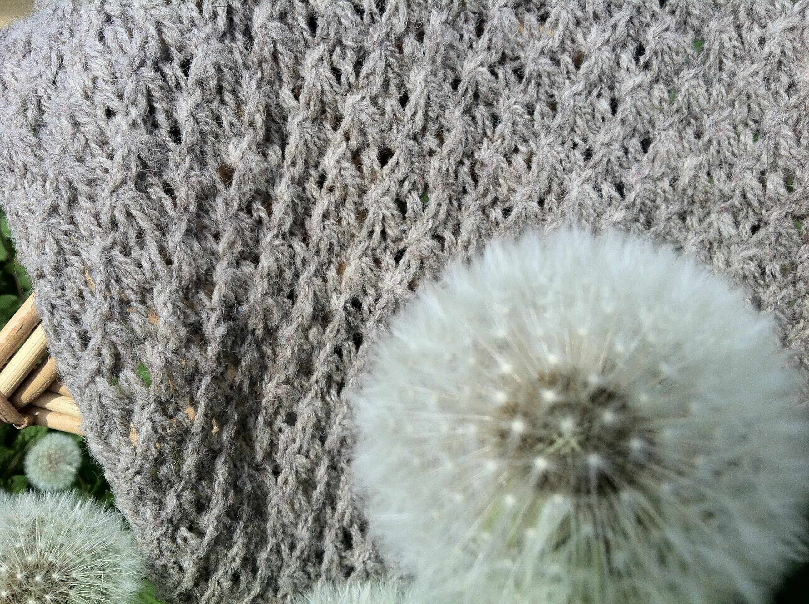 Nahaufnahme von grauem Sternenschal zur Anleitung und Pusteblume davor