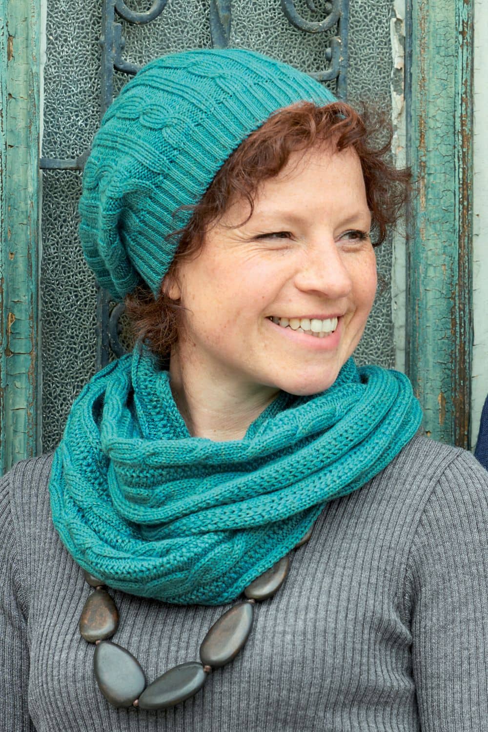 Frau mit grauem Rippshirt trägt Schal und türkise Ballonmütze mit Zopfmuster aus bio Wolle (kbT) vom Finkhof