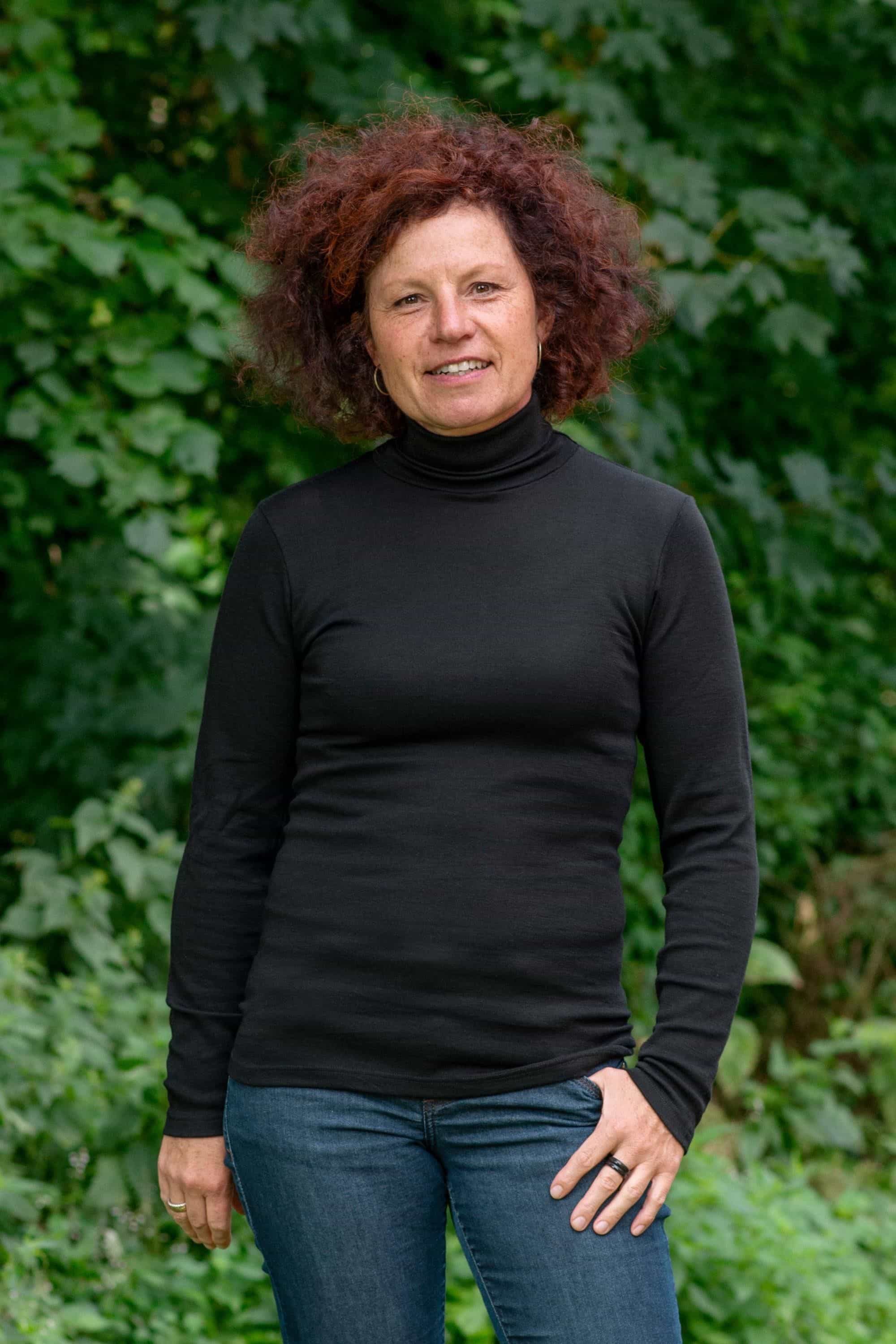 Frau im Garten trägt schwarzes Unterziehshirt mit Rollkragen aus bio Wolle (kbT) und Seide