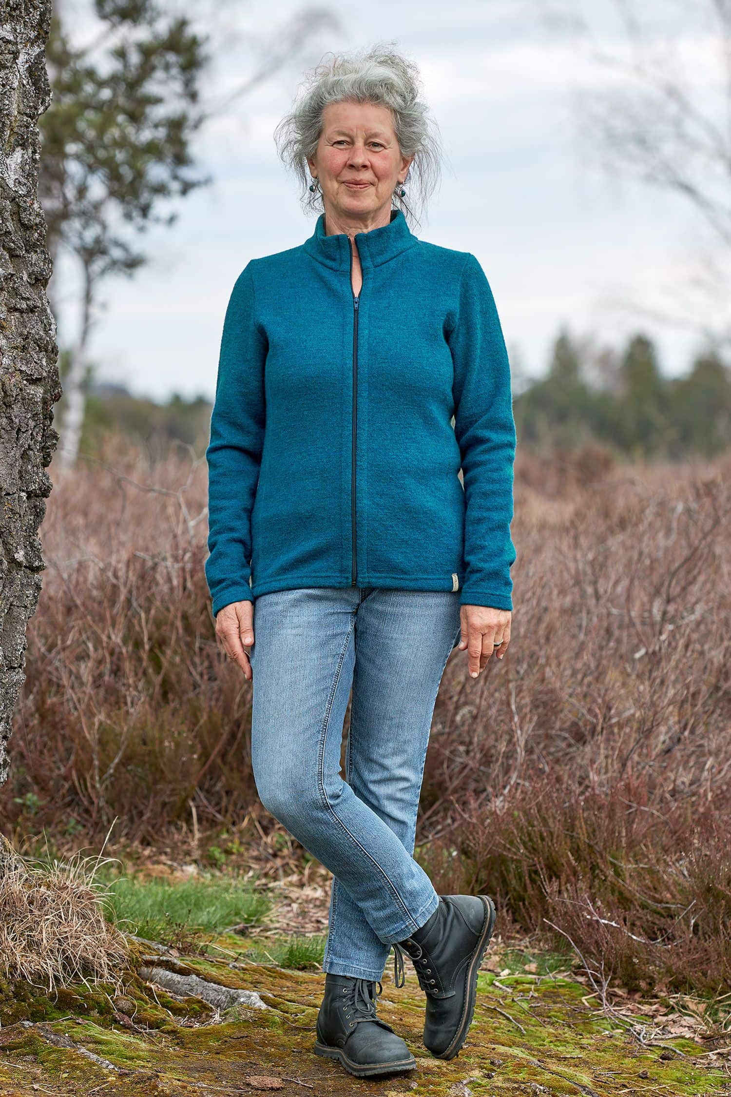 Frau steht im Wald und trägt Jeans und türkise gewalkte Jacke