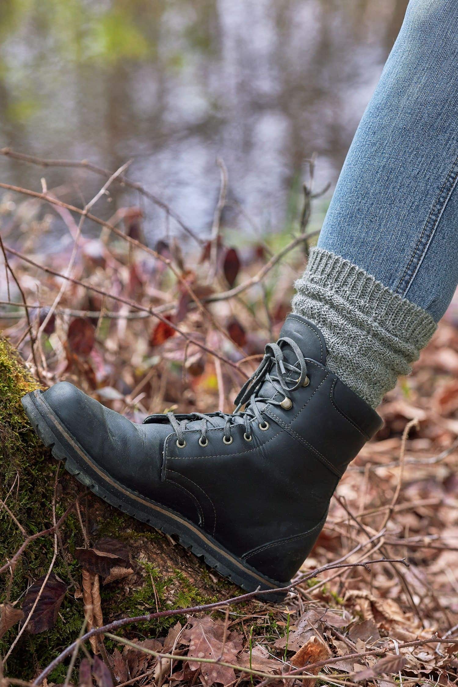 Person stellt Fuß auf Moos und trägt graue Struktursocken aus bio Wolle (kbT) vom Finkhof mit schwarzen Stiefeln und Jeans