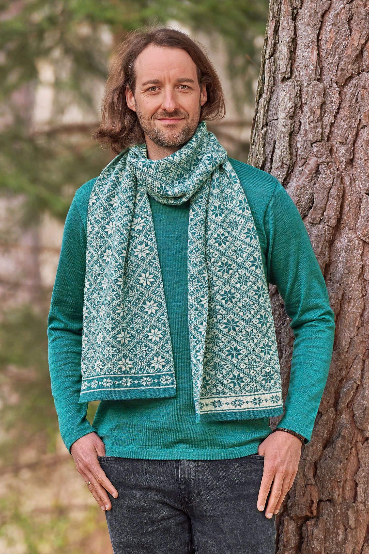 Mann vor Baum trägt türkises Shirt und Wollschal mit winterlichem Muster aus bio Wolle (kbT)