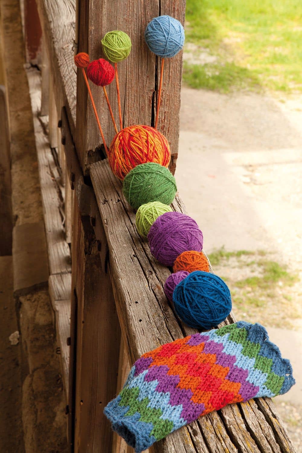 dünne bunte Finkhof Wollknäule aus bio Merinowolle (kbT) und Stulpen mit Muster liegen auf Balkongeländer