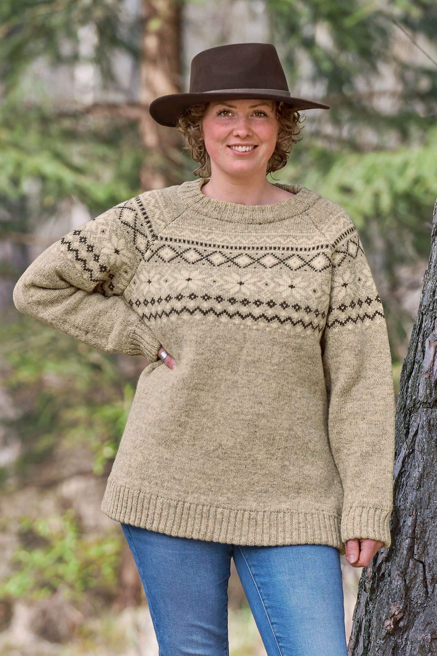 Frau mit Hut steht neben Baum und trägt grauen Finkhof Norwegerpulli aus bio Wolle (kbT)