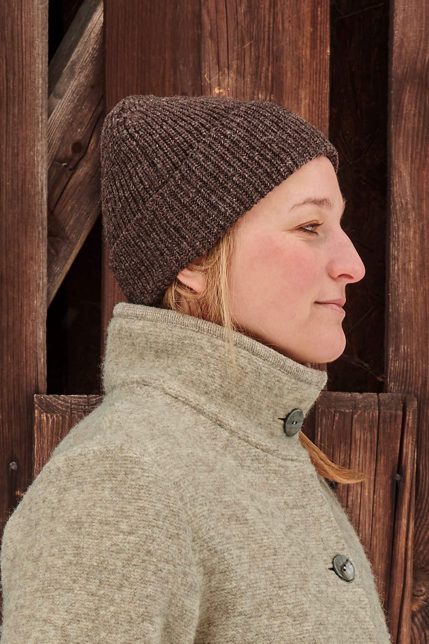 Frau trägt eine braune Finkhof Mütze aus bio Wolle (kbT) und einen Wollwalkmantel vom Finkhof