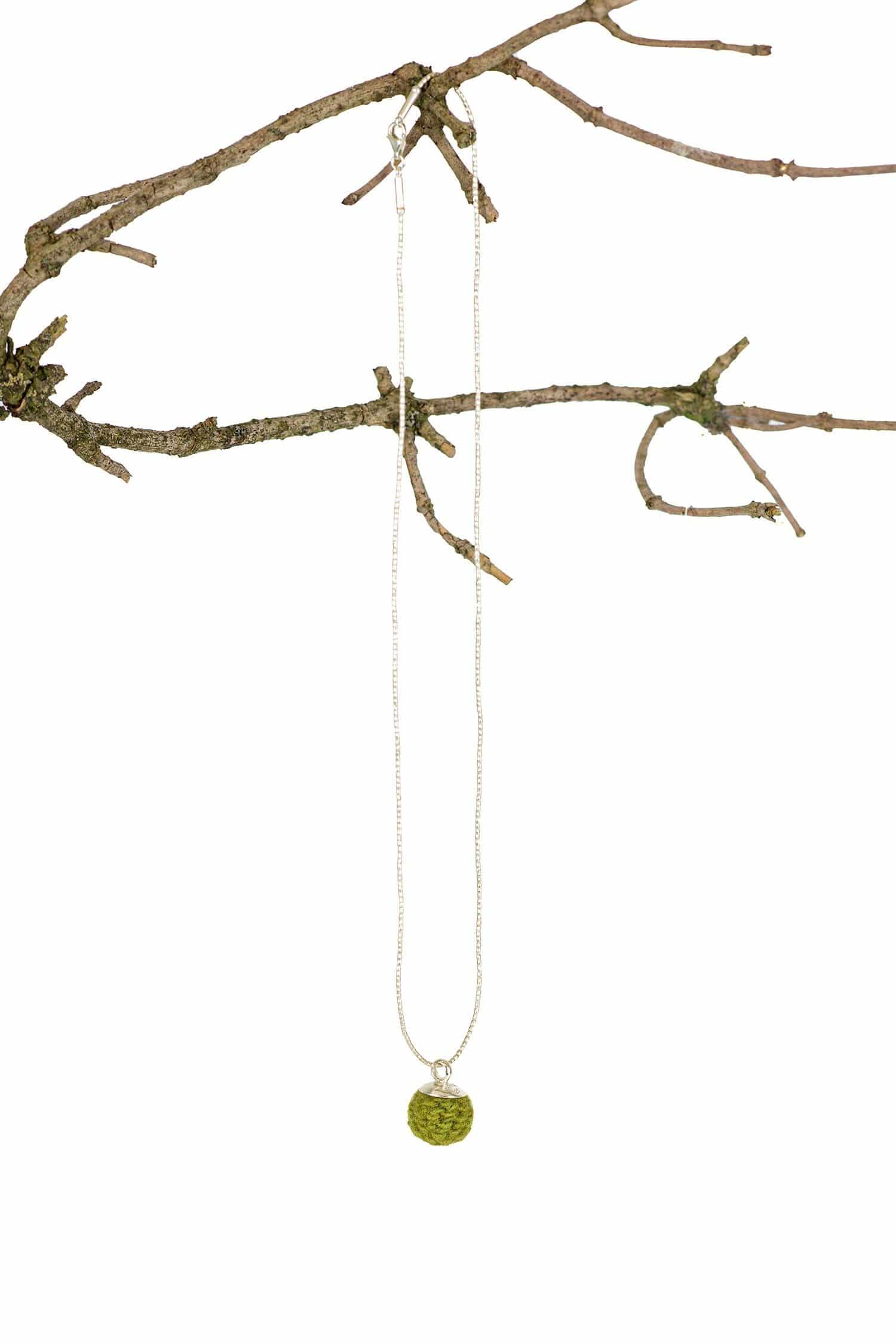 grüne handgemachte Wollperle aus pflanzengefärbter Schurwolle hängt mit einer Kette an einem Ast
