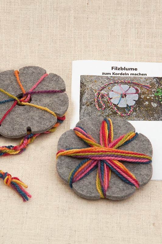 Filzblume graue pflanzengefärbte Filzblume aus bio Wolle (kbT) mit bunten Wollen und Anleitung im Hintergrund