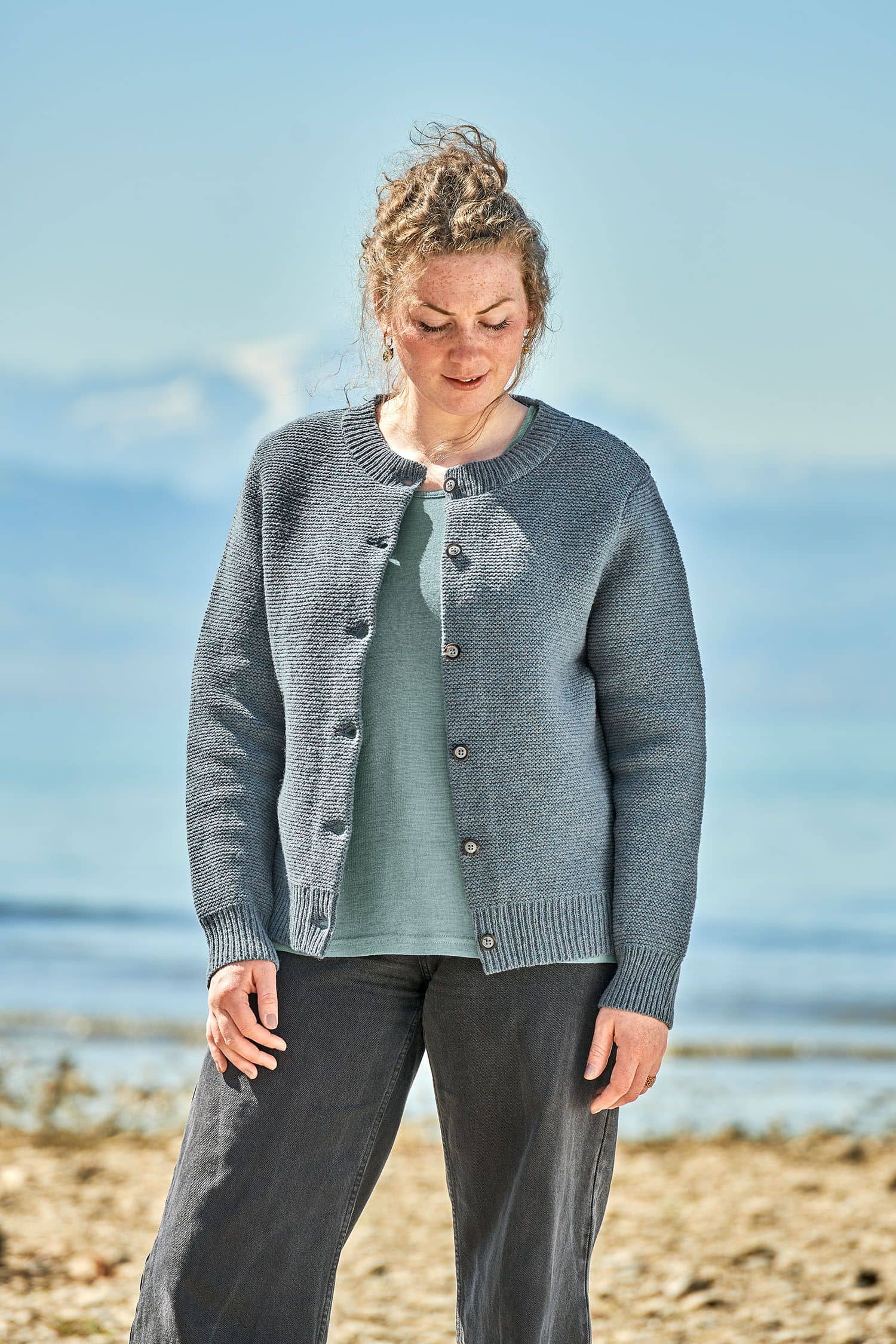 Frau trägt eine schwarze Jeans, ein türkises Shirt und eine rauchblaue Strickjacke vom Finkhof aus bio Merinowolle (kbT)