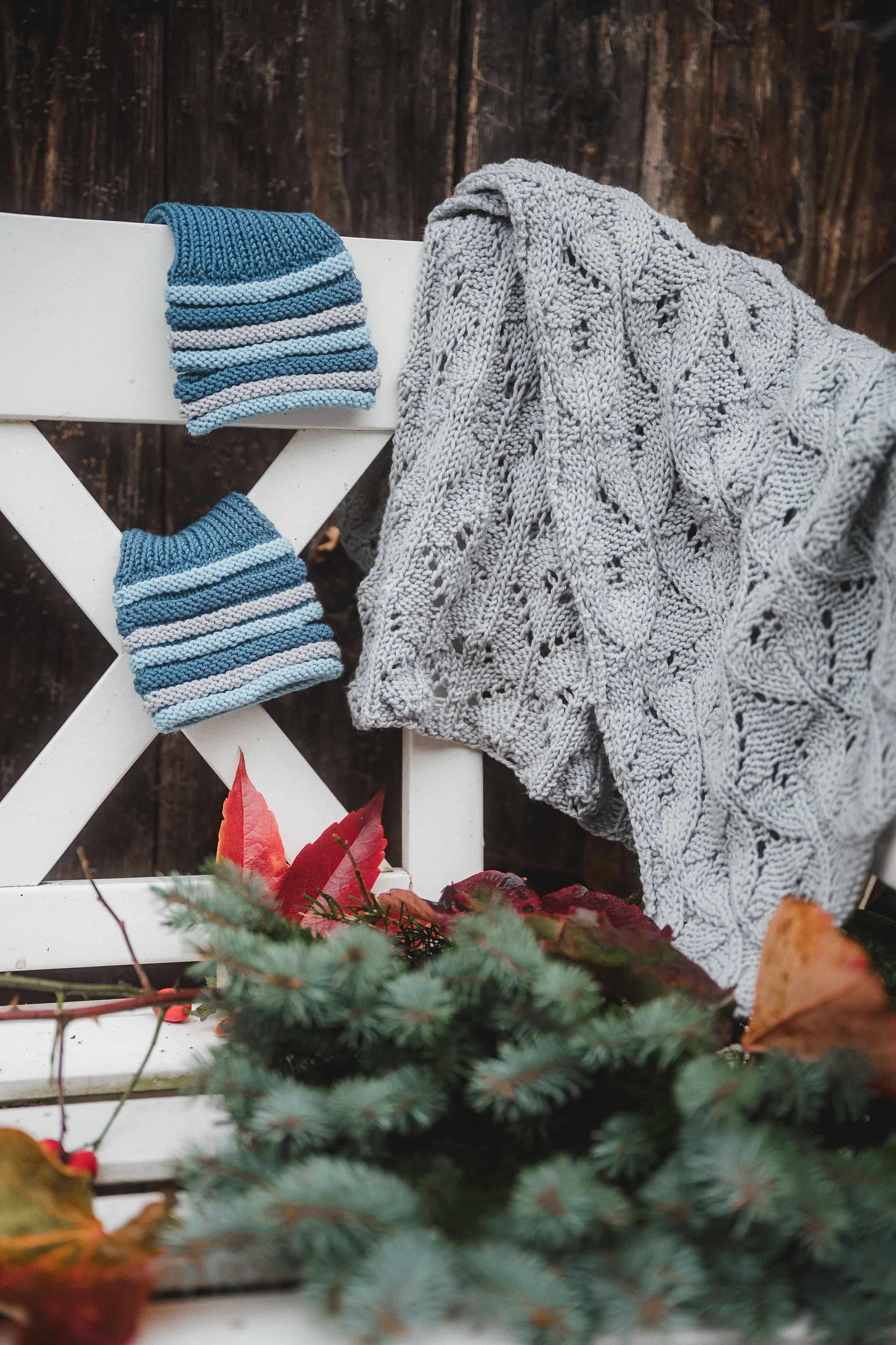 auf einer Bank hängen blaue Stulpen und ein graues Tuch mit Ajourmuster