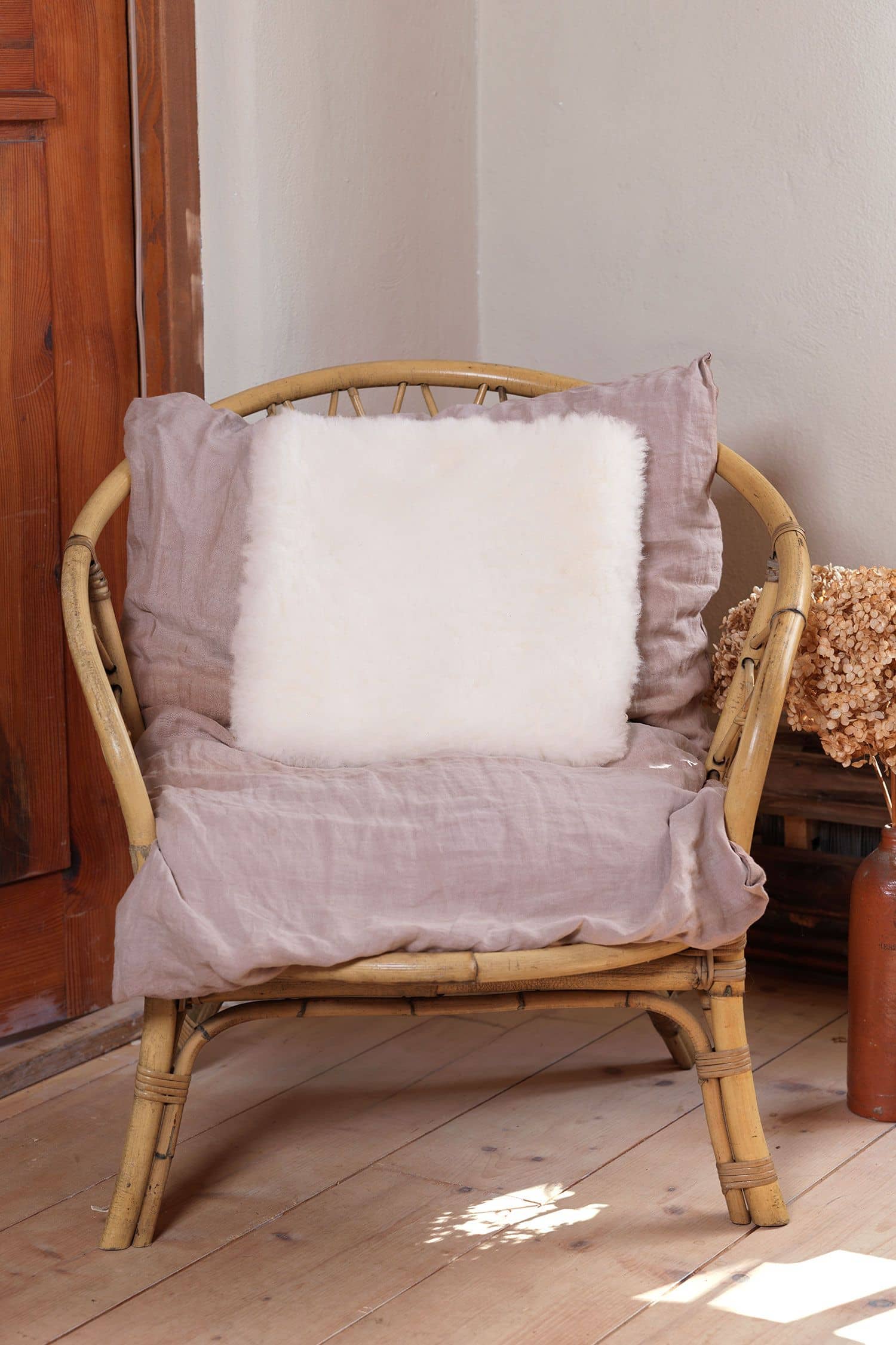 Wohlfühlkissen quadratisch pflanzlich gegerbt weiß quadratisches Wohlfühlkissen aus pflanzlich gegerbtem Finkhof Fell liegt auf einem Korbstuhl