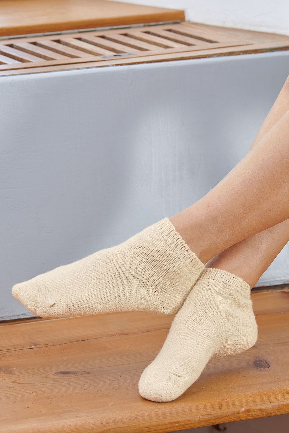 Naturweiße Bettsocken aus Wolle und Seide getragen auf Holzuntergrund