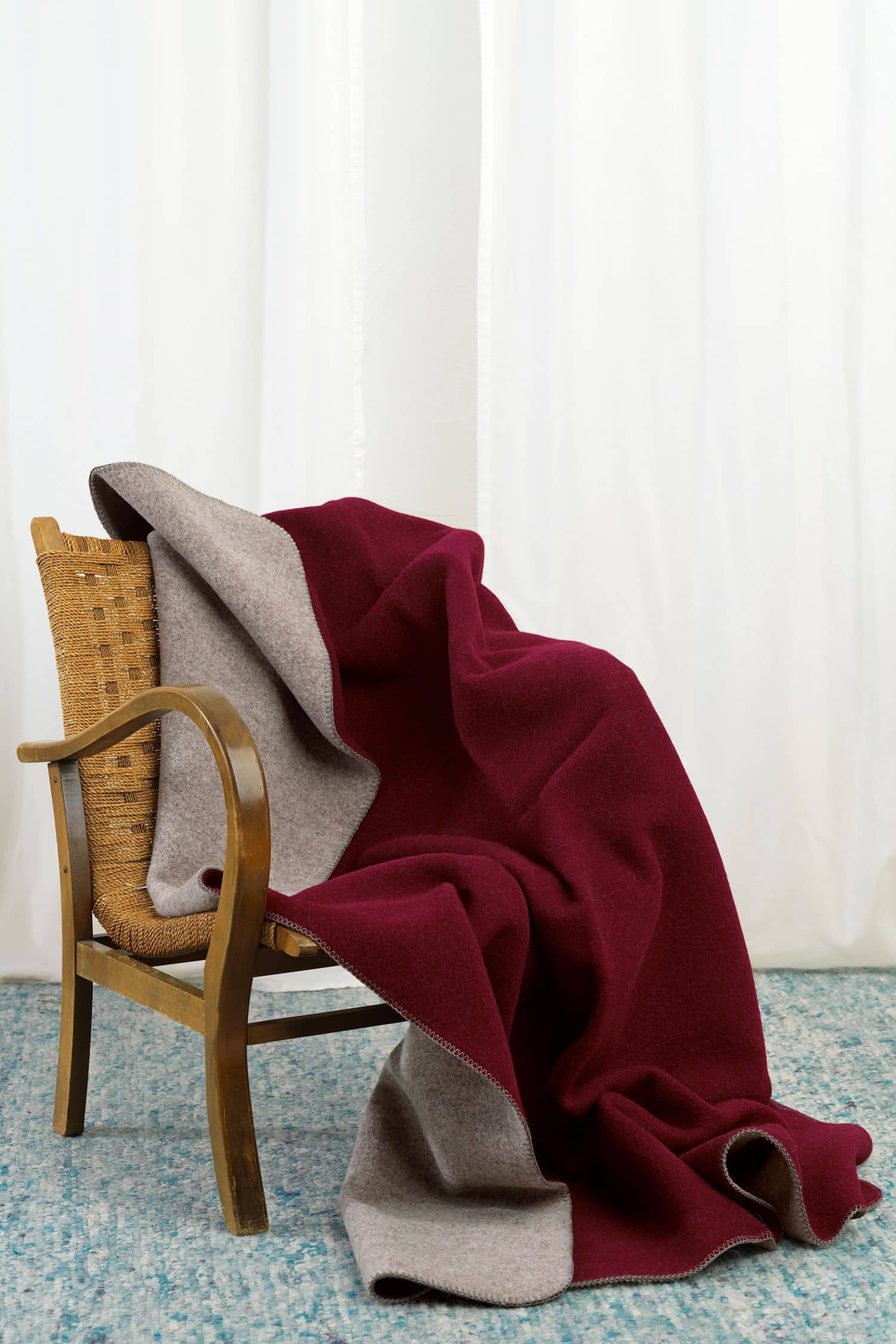 burgunderrote/ graue Finkhof Doubleface Wolldecke aus bio Wolle (kbT) vom Merinolandschaf über Korbstuhl gelegt