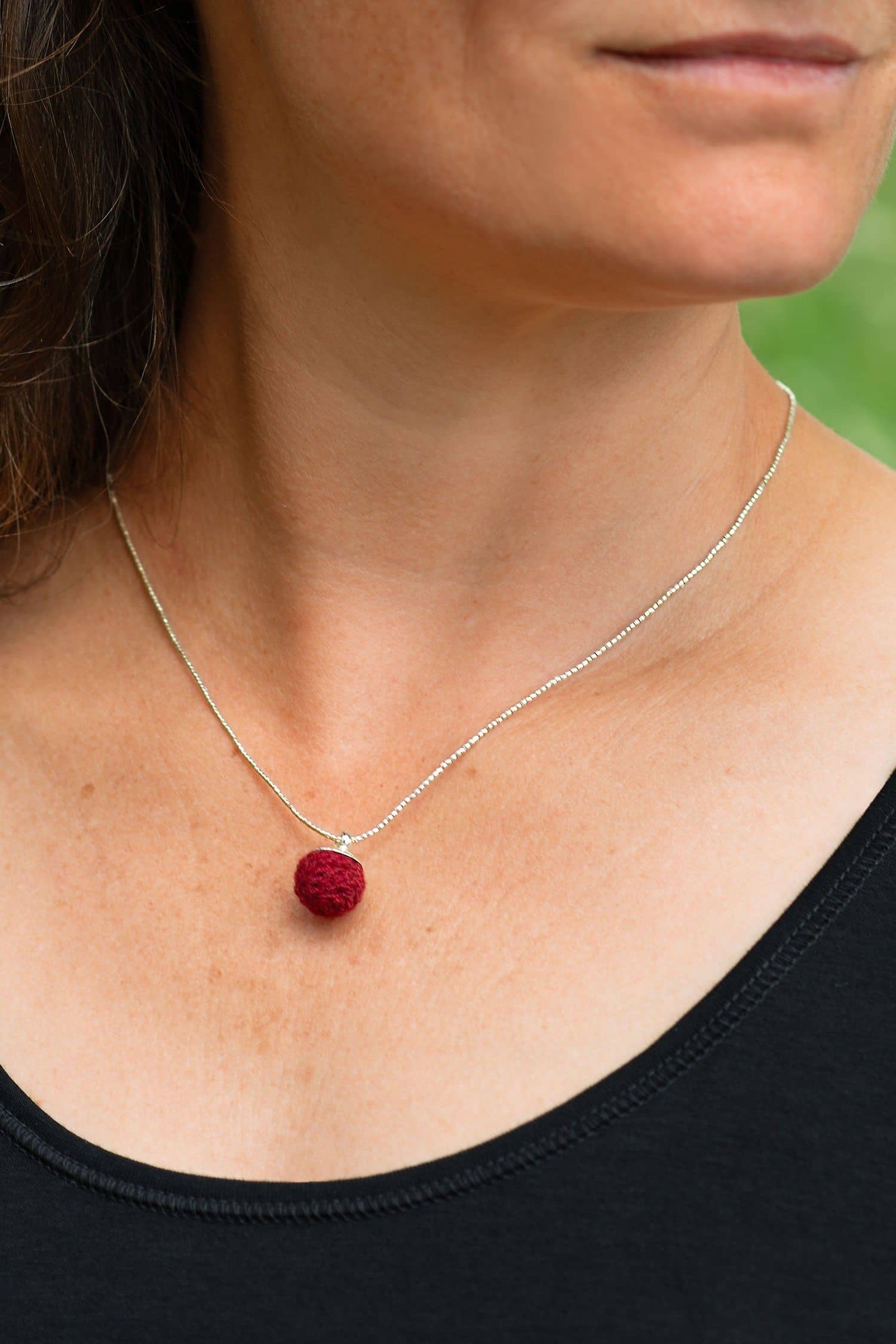 Frau trägt silberne Kette mit purpurrotem Kettenanhänger in Form einer Perle