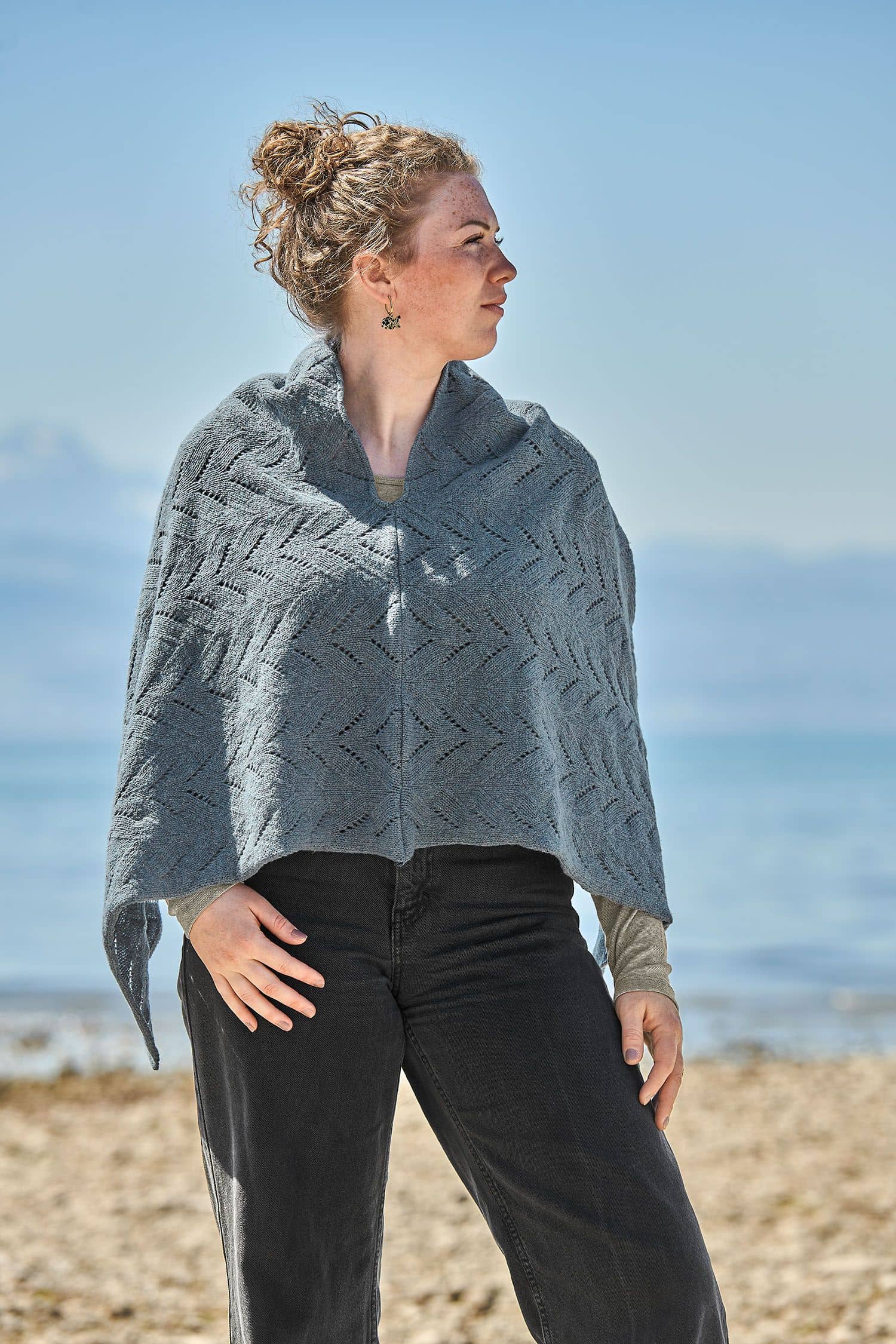 Frau trägt eine schwarze Jeans und einen rauchblauen Poncho mit Ajour Muster vom Finkhof aus bio Merinowolle (kbT)