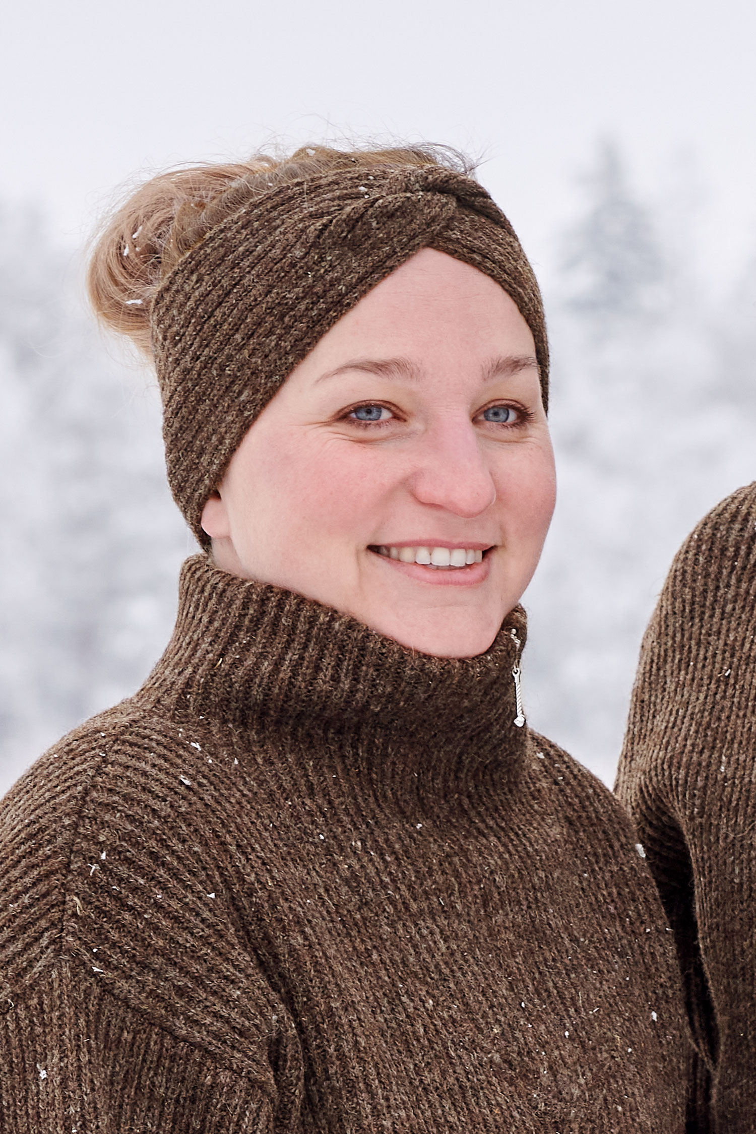 Frau trägt braunes Finkhof Stirnband mit Twist aus bio Wolle (kbT) und einen braunen Finkhof Troyer