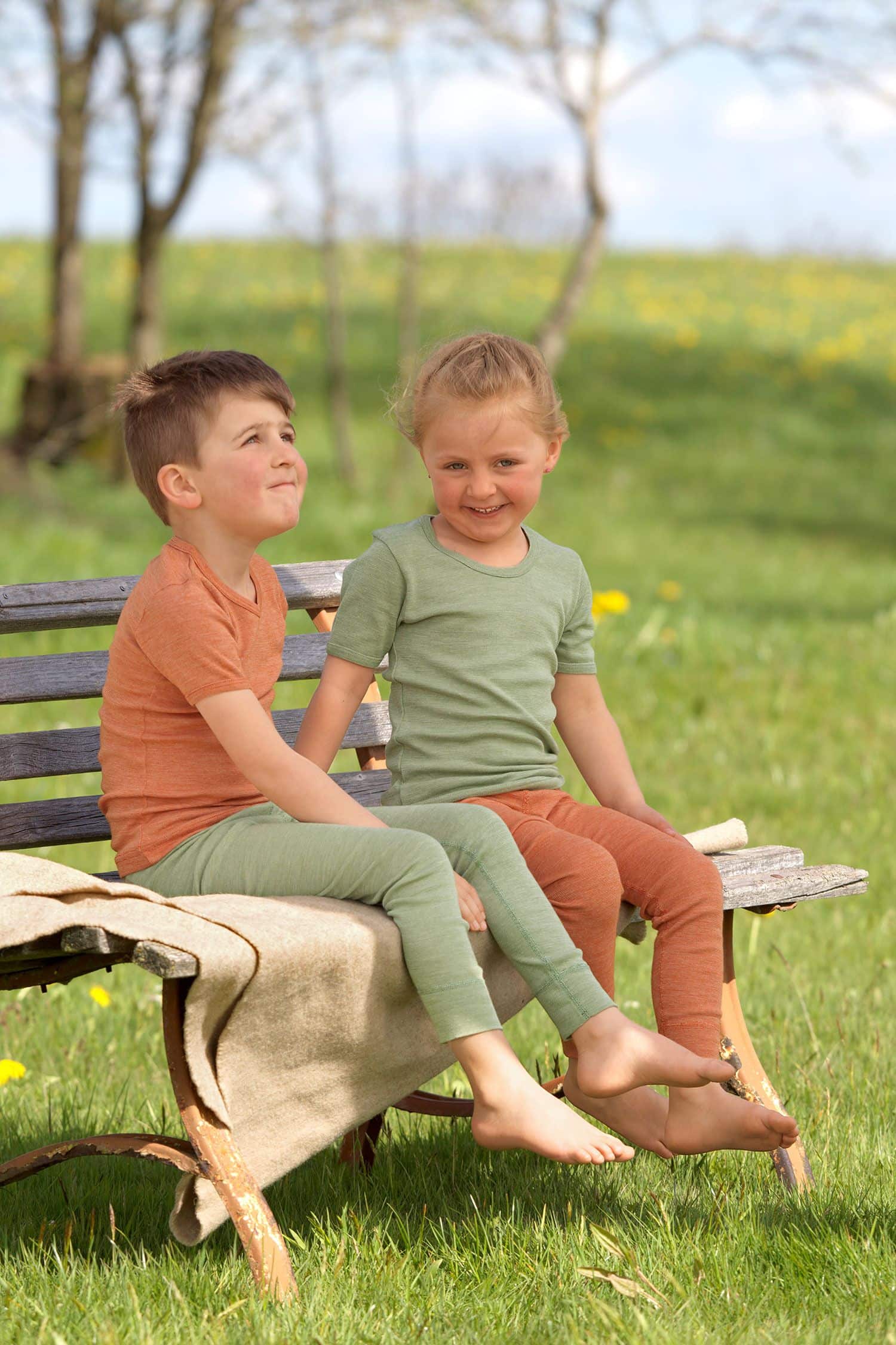 Wollmix Kinder-Kurzarmshirt - Baumwolle-Wolle-Seide Kinder sitzen auf Bank mit Fell und tragen lange Unterwäsche aus bio Wolle (kBT), bio Baumwolle (kbA) und Seide