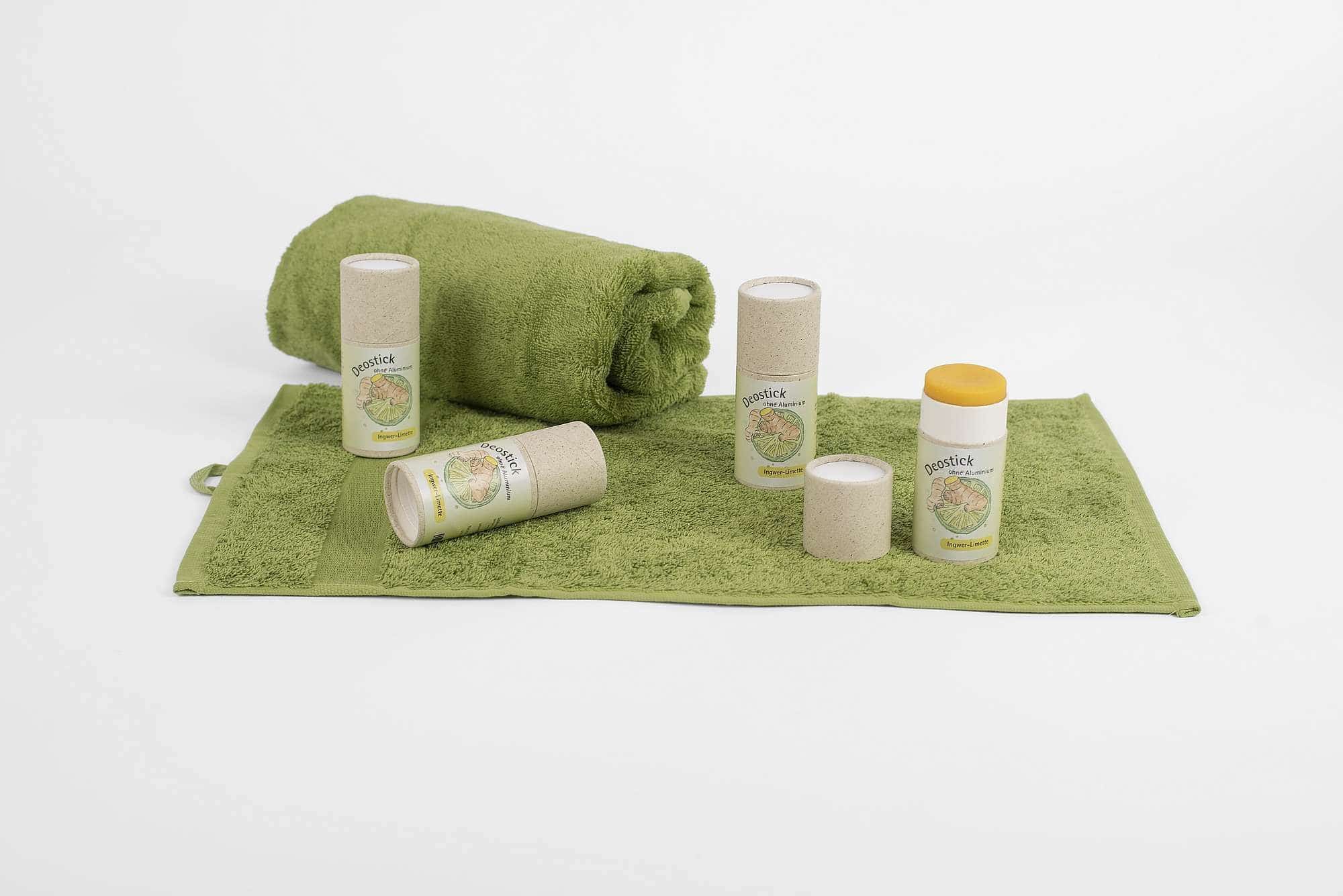 s157-6070100-deostick-graspapier-3717 Deostick in brauner Pappverpackung mit Inger-Limetten Duft auf grünem Handtuch verstreut, einer ist offen