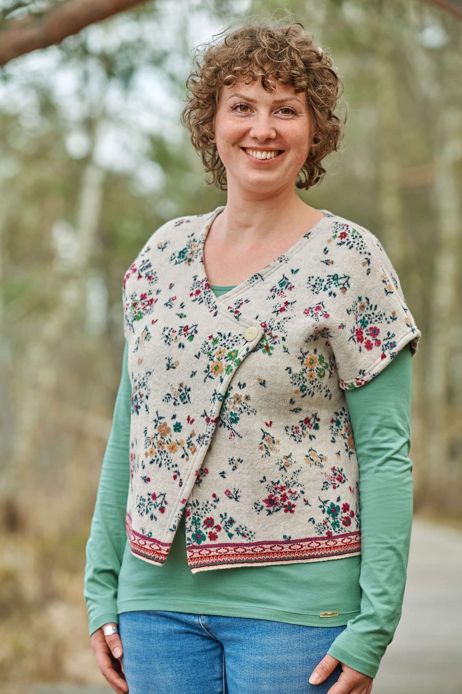 Frau mit schilfgrünem Shirt trägt weiße gemusterte Weste ohne Ärmel aus bio Merinowolle (kbT) und bio Baumwolle (kbA)