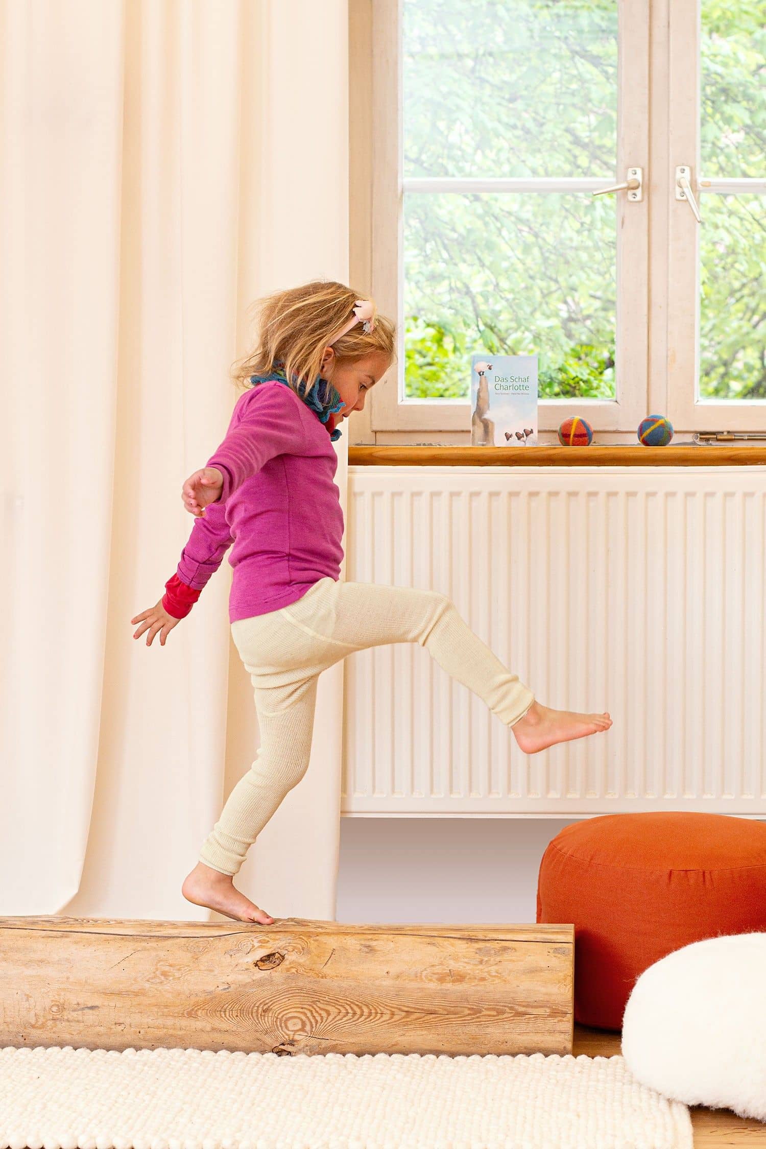 Kind spielt auf Stamm und trägt pinkes Shirt, bunten Schal und naturweiße Woll-Leggings aus bio Wolle (kbT)