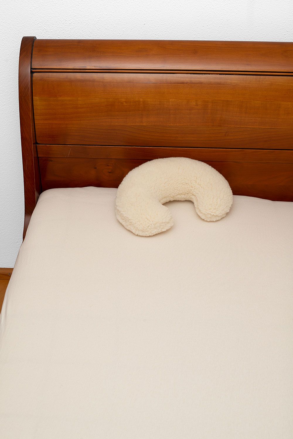 naturweißes Nackenhörnchen vom Finkhof mit Wollplüschbezug aus bio Wolle (kbT) auf hellem Laken in Holzbett