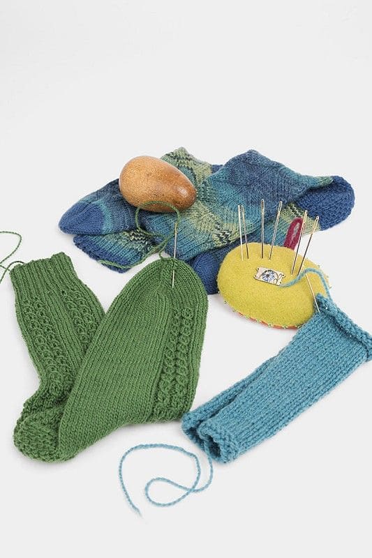 Stopfnadeln Stopfnadeln aus Metall sind in Nadelkissen gesteckt, rundherum liegen Stricksocken und Stopfei