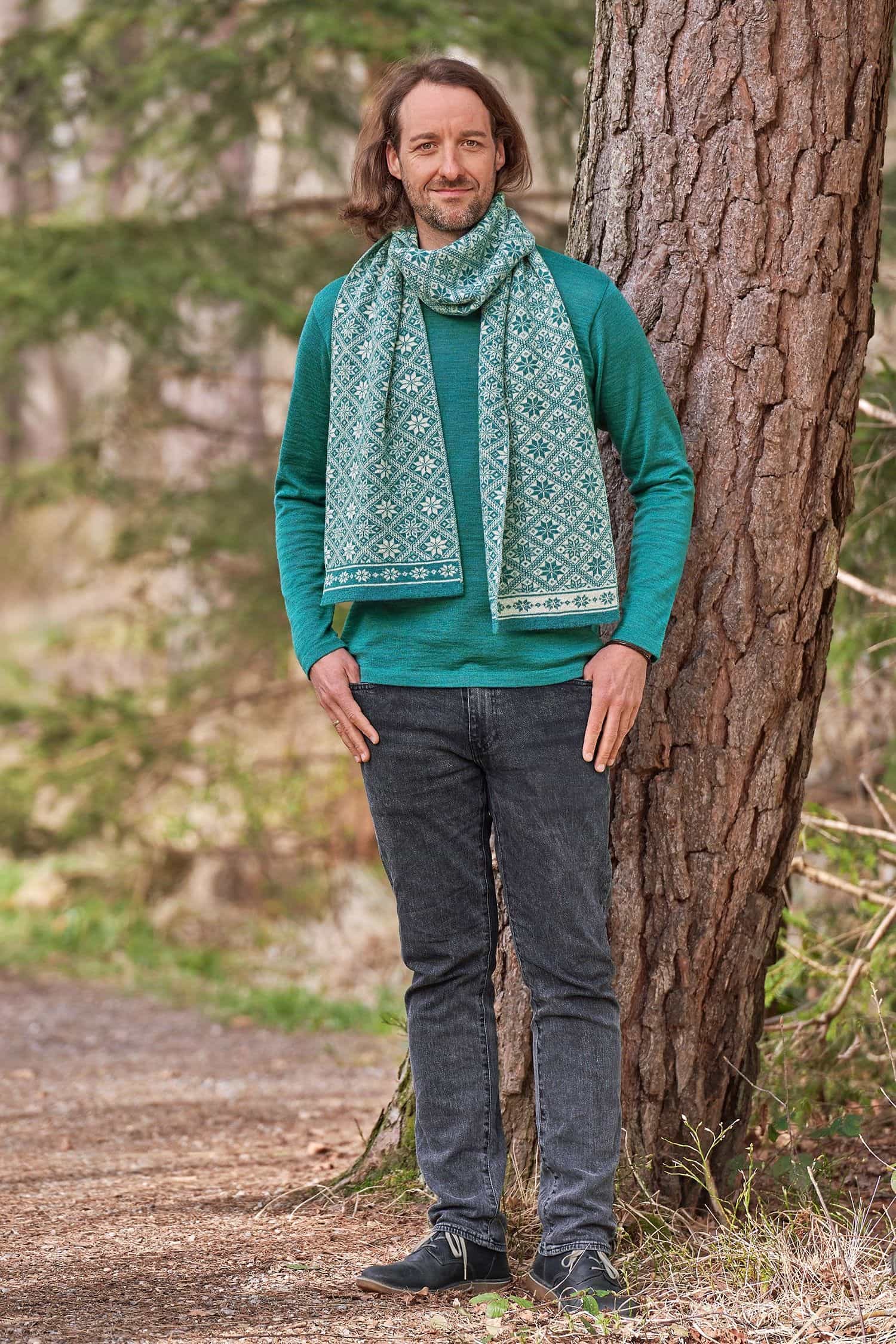 Mann steht vor Baum und trägt petrolblaues Wollshirt aus bio Wolle (kbT) vom Finkhof mit türkis gemustertem Schal