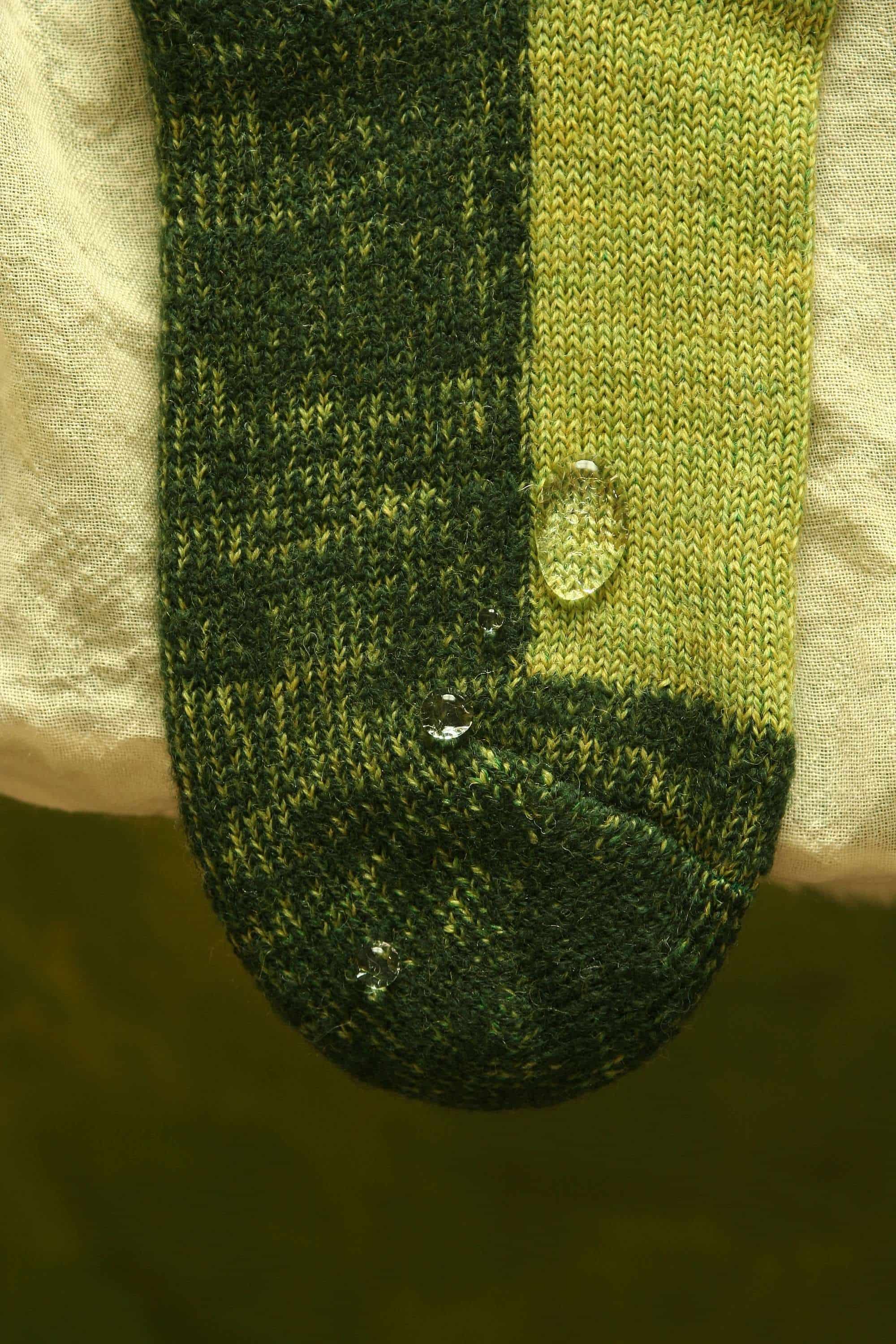 Nahaufnahme von abperlenden Wassertropfen auf grüner Trekking-Socke aus bio Wolle (kbT) und bio Baumwolle (kbA)