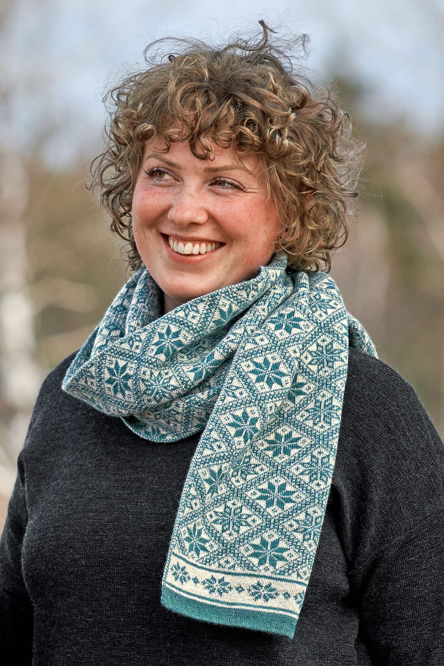 Frau mit dunkelgrauem Shirt trägt türkisen Schal mit winterlichem Muster aus bio Wolle (kbT)