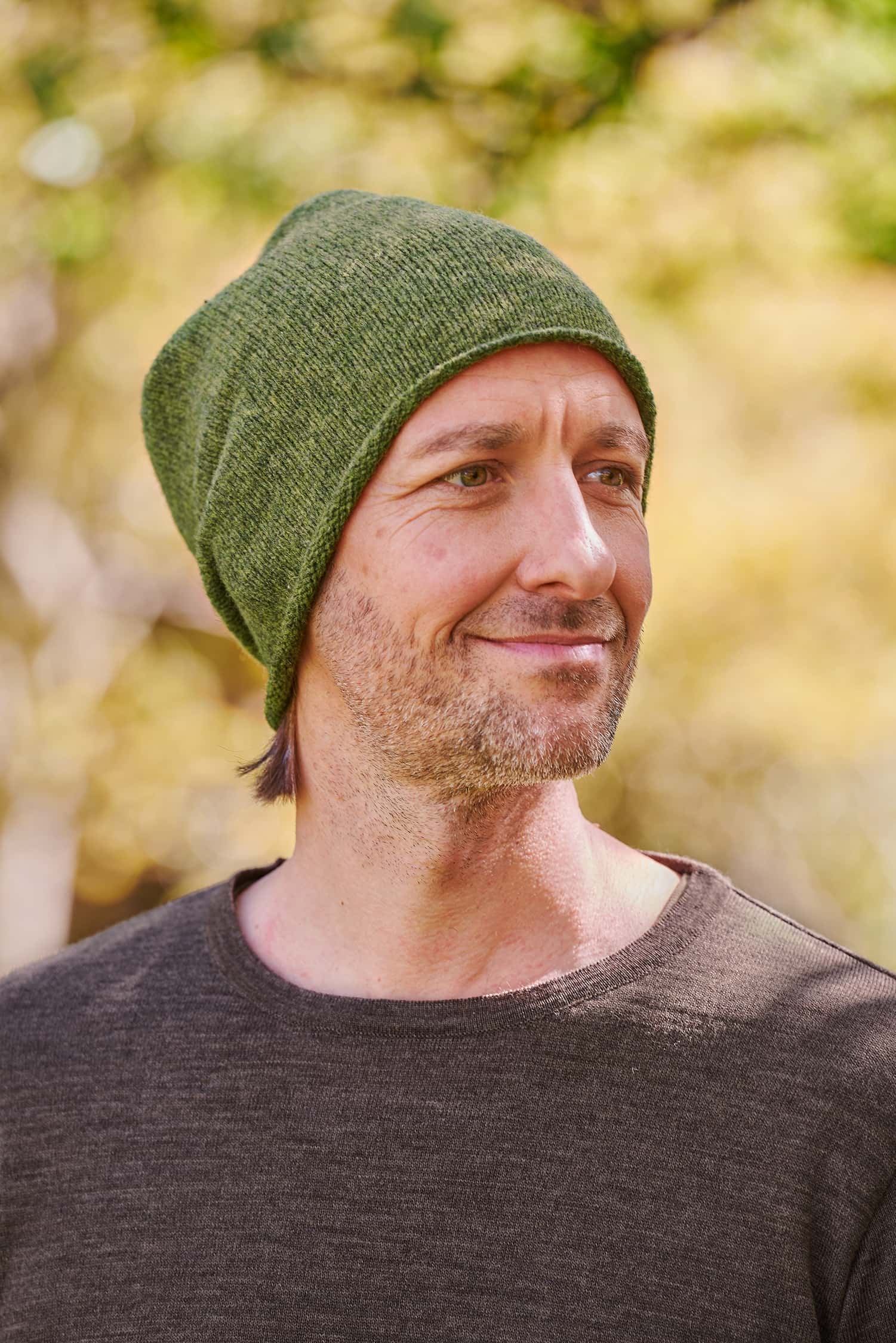 Mann trägt eine grüne Strickmütze mit Rollrand vom Finkhof aus Bio-Wolle und ein braunes Shirt