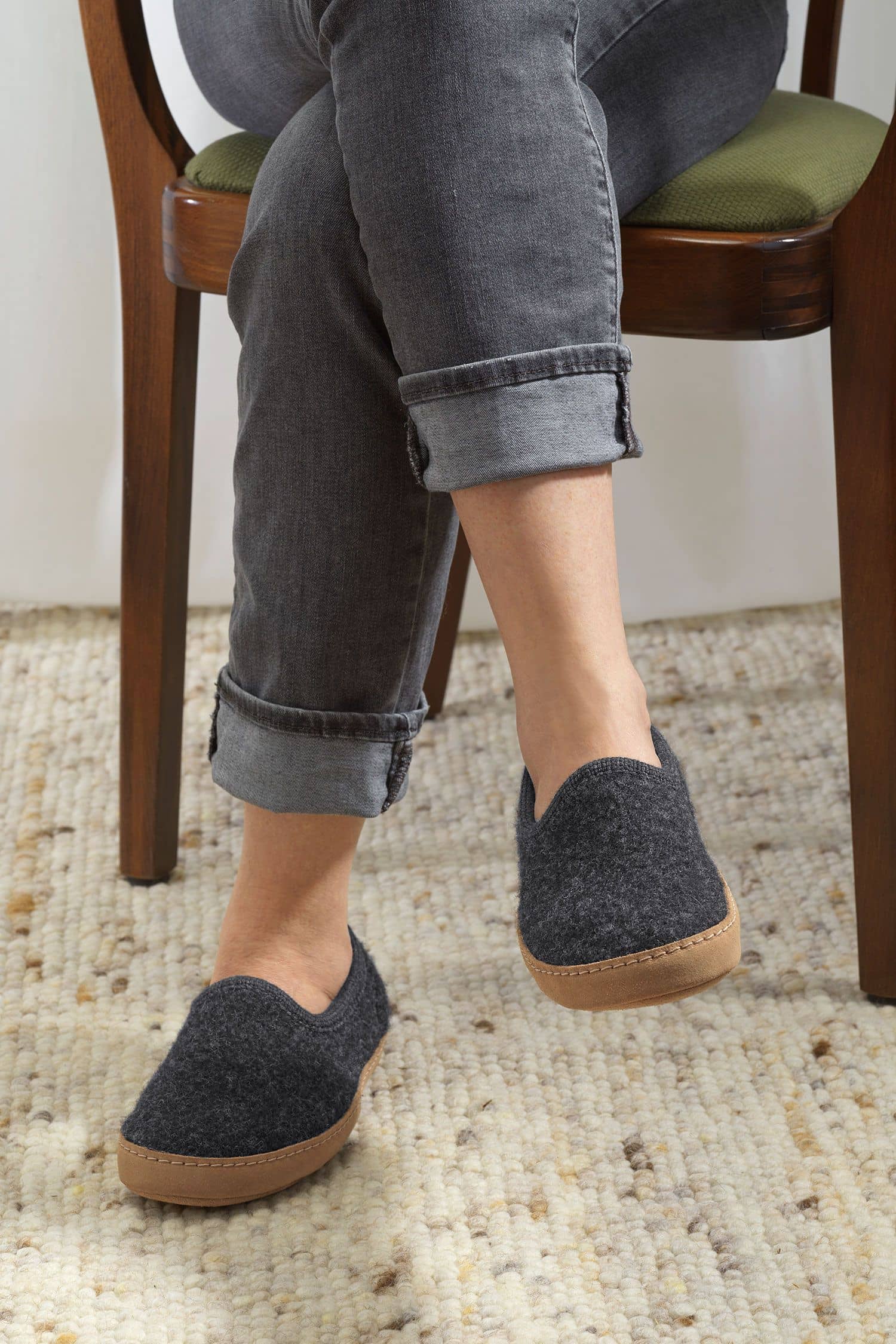 Person trägt anthrazitfarbene Finkhof Hausschuhe aus bio Wolle (kbT) mit einer Sohle aus pflanzlich gegerbtem Rindsleder