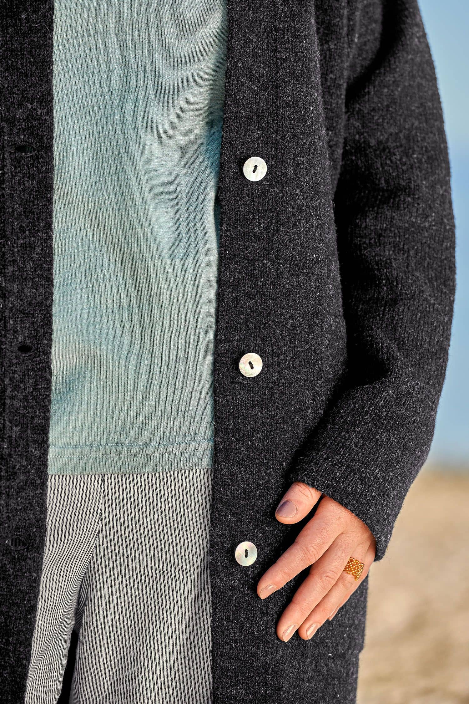 Frau trägt anthrazitgrauen Strickmantel aus bio Wolle (kbt) vom Finkhof, ein blaues Shirt und eine Stoffhose