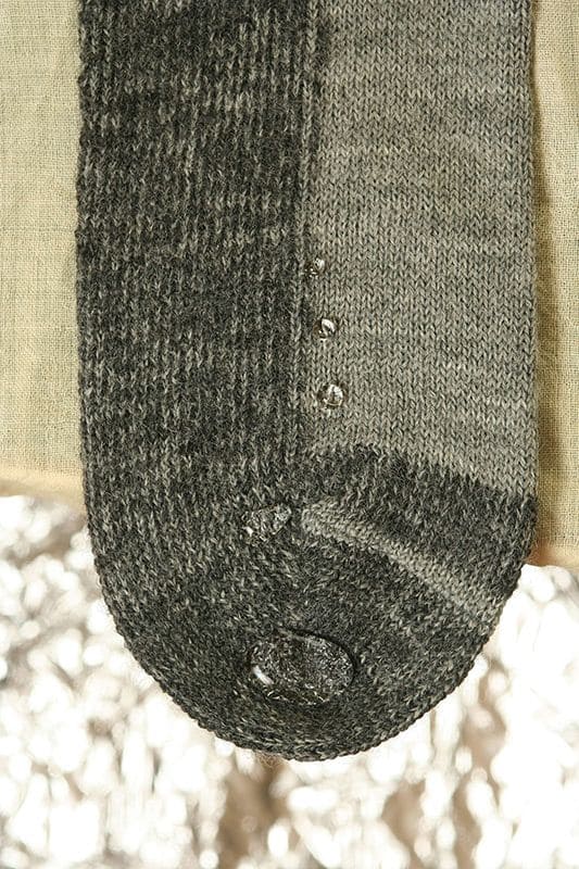 Nahaufnahme von abperlenden Wassertropfen auf grauer Trekking-Socke aus bio Wolle (kbT) und bio Baumwolle (kbA)