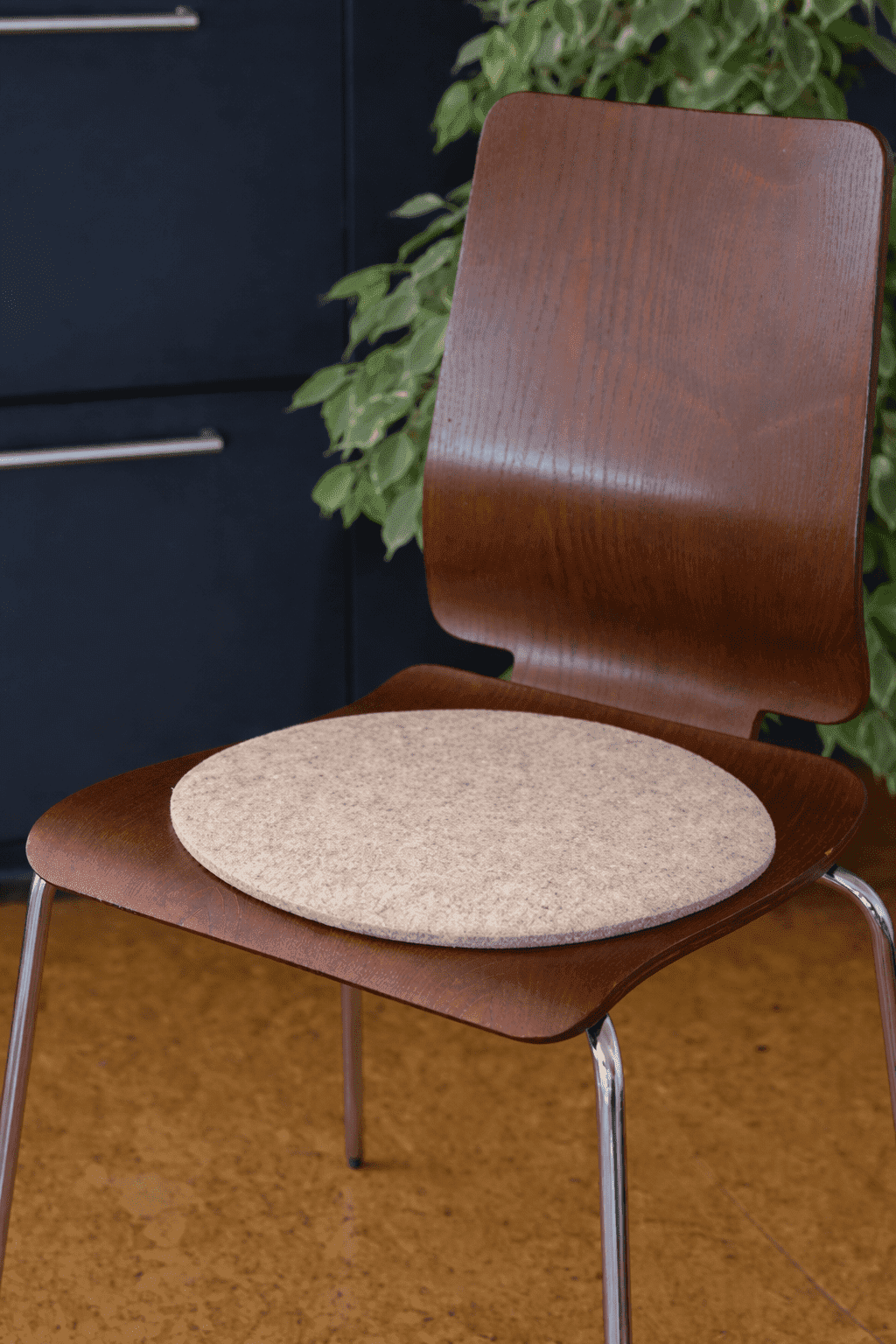 runde Finkhof Sitzauflage in grau aus bio-Schurwolle (kbT) auf einem Holzstuhl in einer schwarzen Küche