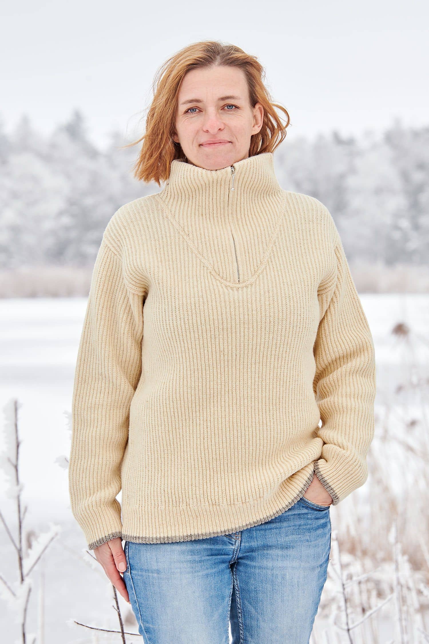 Frau in Schneelandschaft trögt einen naturweißen Finkhof Troyer aus bio Wolle (kbT)