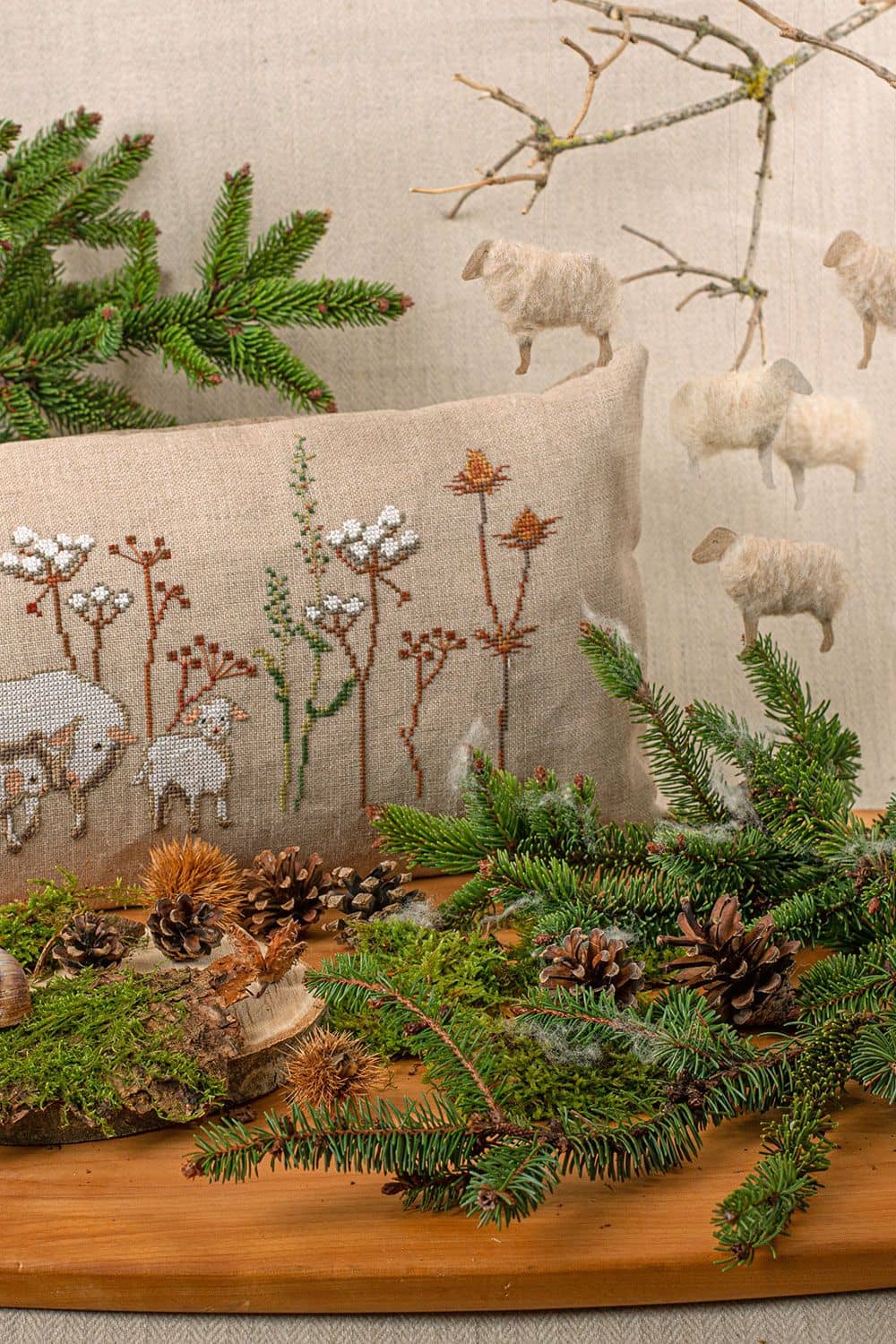 Beispielprojekt zum Buch ,,Winterfreuden" mit besticktem Kissen, Tannenzapfen, Zweigen und hängenden Wollschäfchen