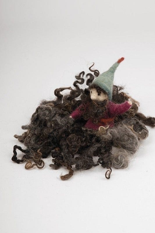 Zwerg mit roter Jacke und grüner Mütze sitzt in graubraunen Wolllocken