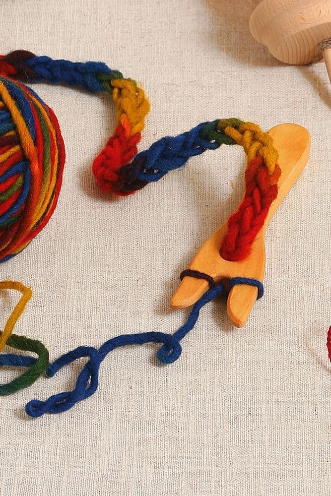 Strickgabel Strickgabel aus Holz mit Strickstück aus bunter Wolle auf beigem Untergrund