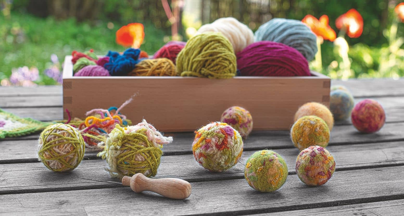 Filzkugeln in verschiedenen Größen und im Hintergrund eine Kiste mit Wollen in verschiedenen Farben