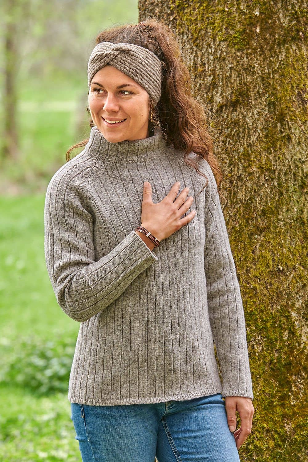 Finkhof-Raglanpullover Frau steht vor Baum und trägt grauen Finkhof Reglanpullover aus bio Wolle (kbT) mit passendem Stirnband