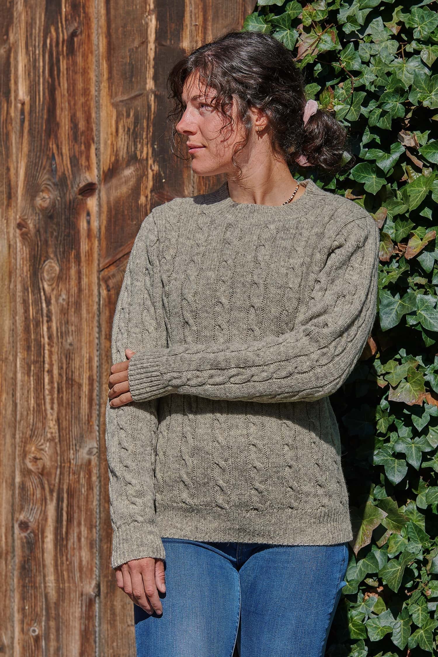 Frau trägt grauen Wollpullover vom Finkhof mit Zopfmuster aus Bio-Wolle dazu Jeans und Stiefel