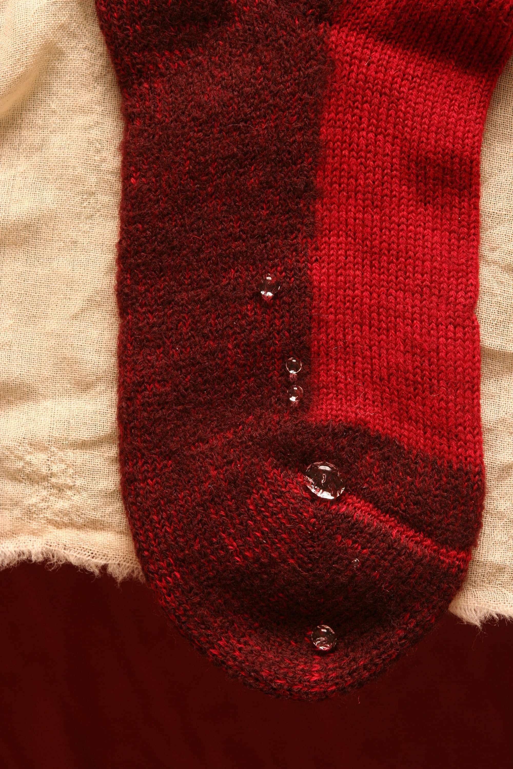 Nahaufnahme von abperlenden Wassertropfen auf roter Trekking-Socke aus bio Wolle (kbT) und bio Baumwolle (kbA)