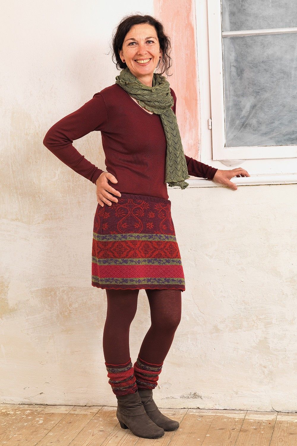 Frau mit rotem Shirt und grünem Schal trägt rot gemusterte Beinstulpen und Cacheur aus bio Wolle (kbT)